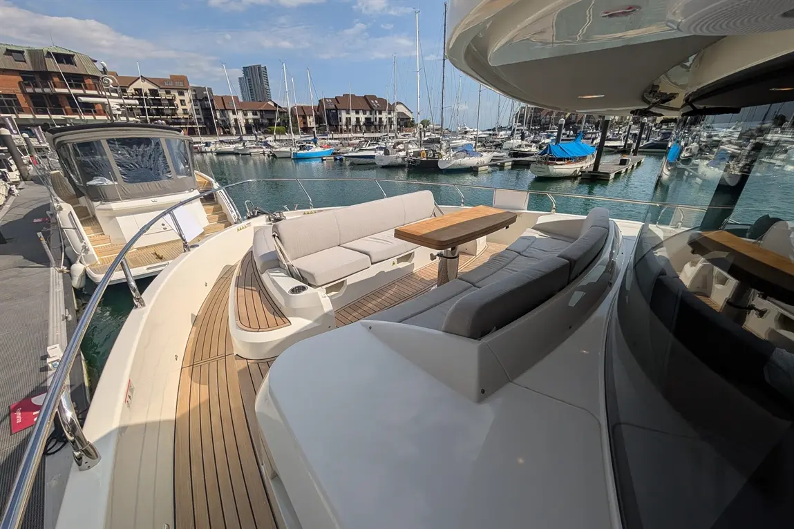 Luxury yacht deck with grey seating and wooden table overlooking a marina filled with boats and waterfront buildings.